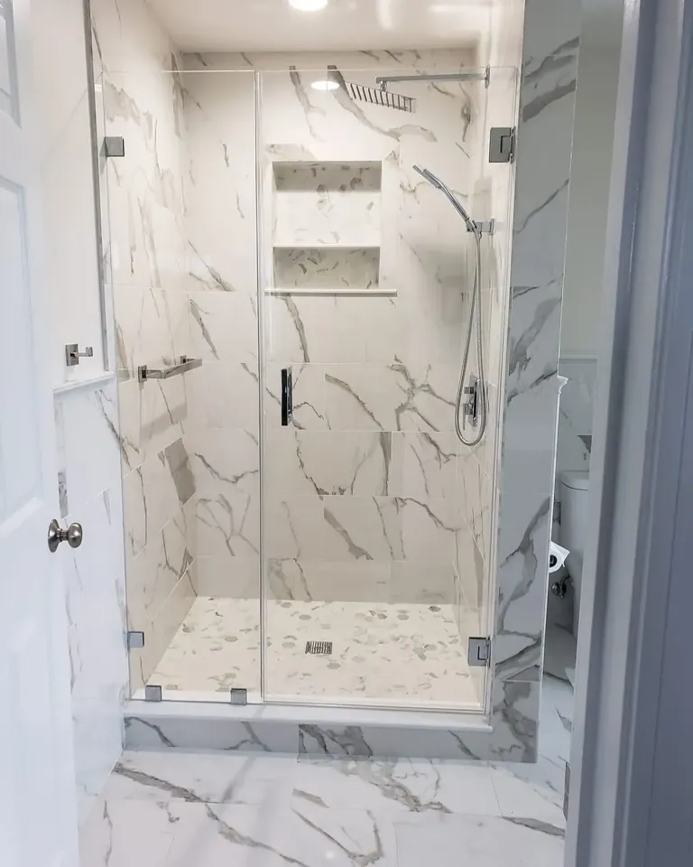 Glass shower door beside marble-patterned tile